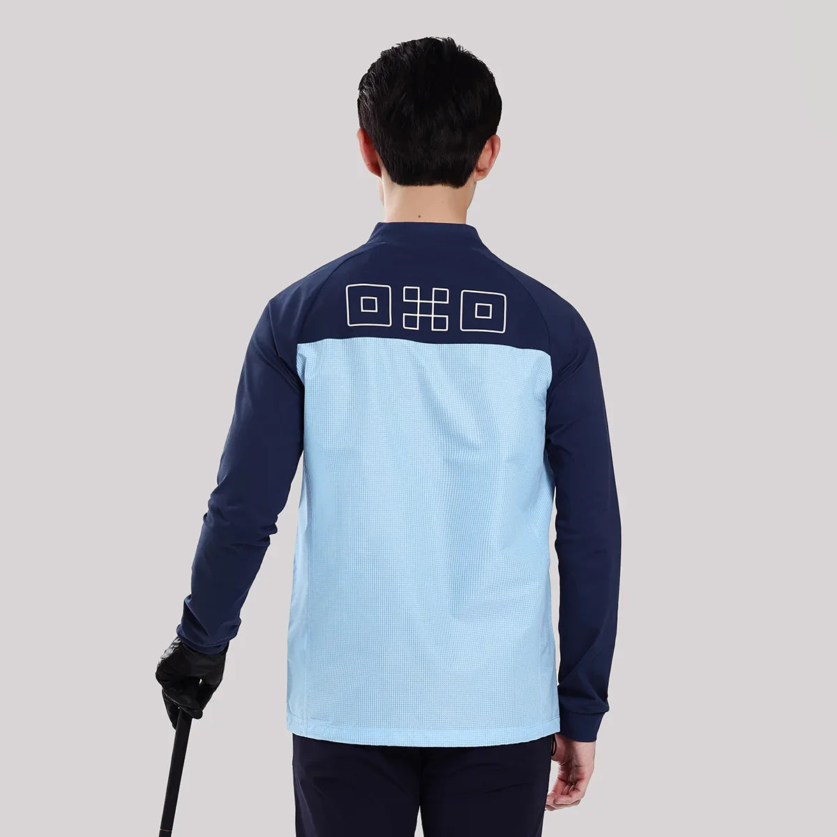 Person wearing a blue and navy long-sleeve shirt with a logo on the back, holding a golf club.
