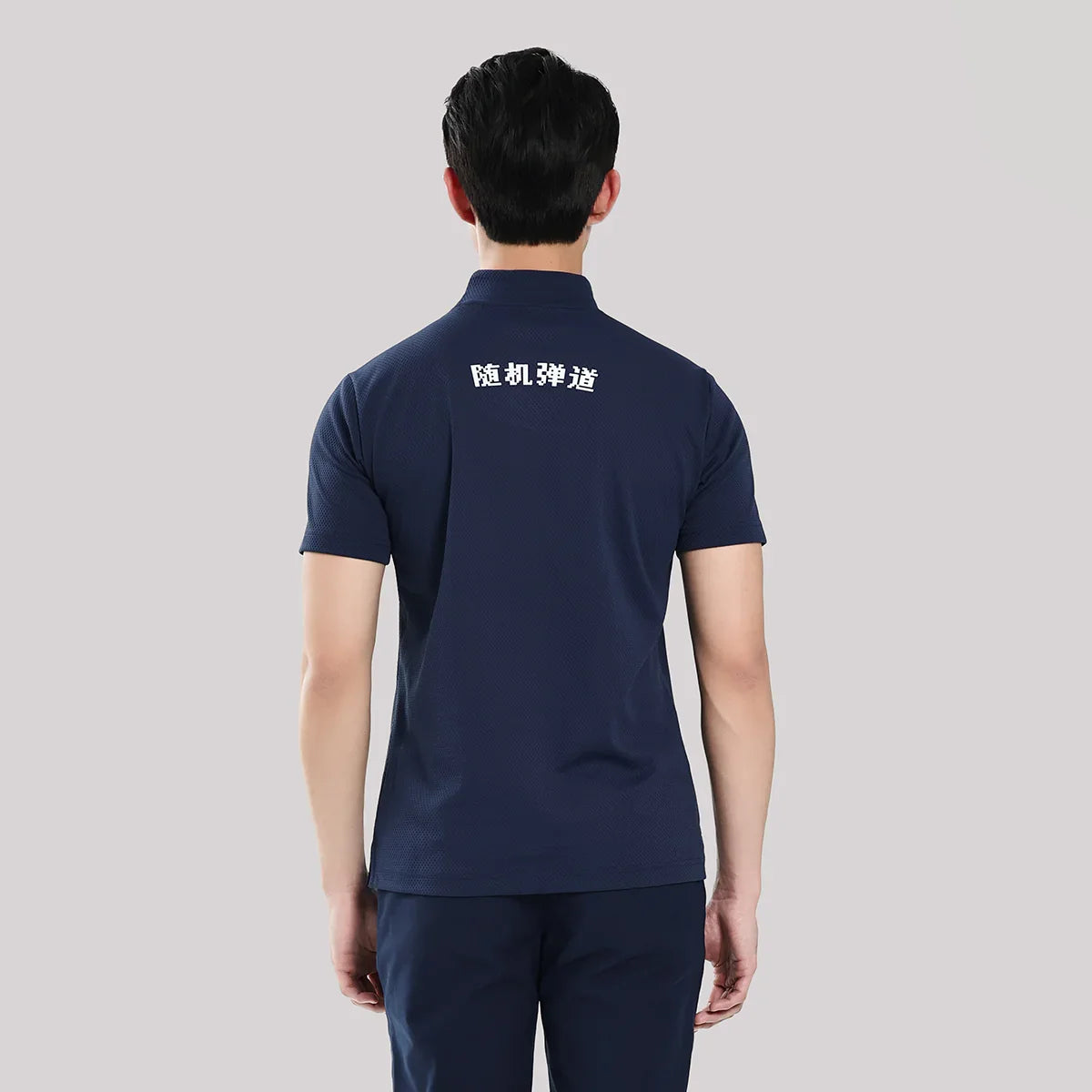 Person wearing a navy blue polo shirt with white text on the back against a gray background