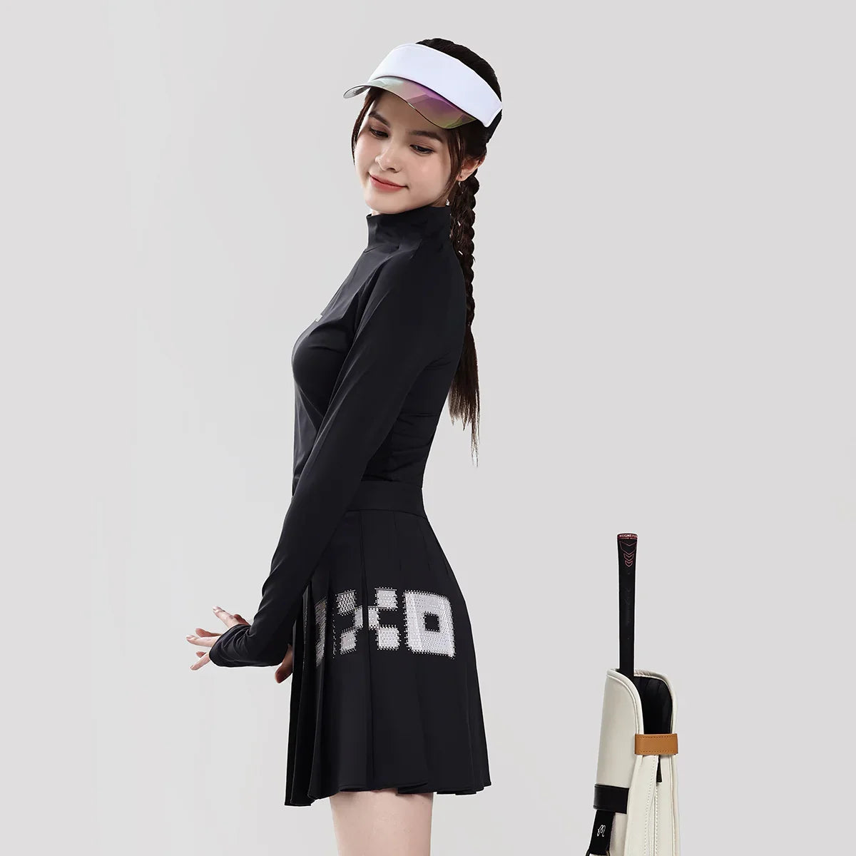 Woman in black tennis outfit with visor and racket on a light gray background