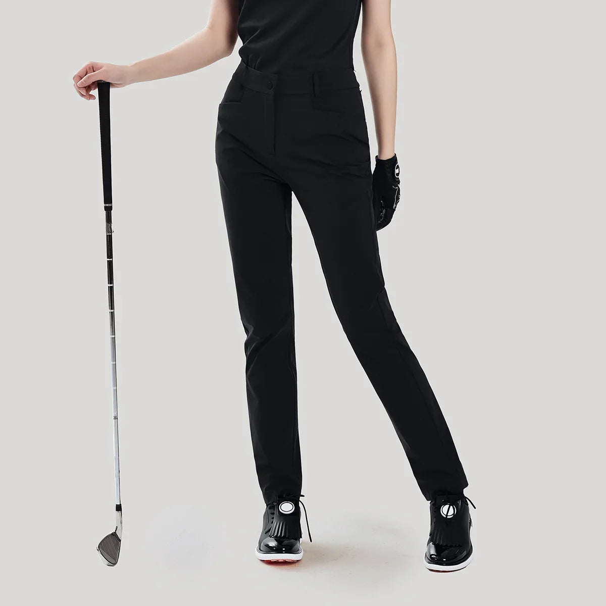 Person wearing black golf pants holding a golf club on a light gray background