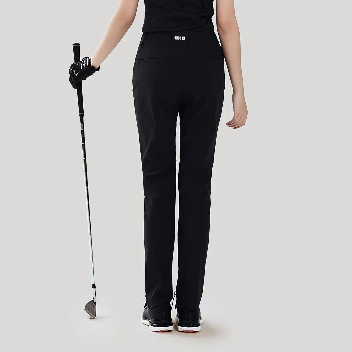 Person wearing black golf pants with a golf club on a light gray background