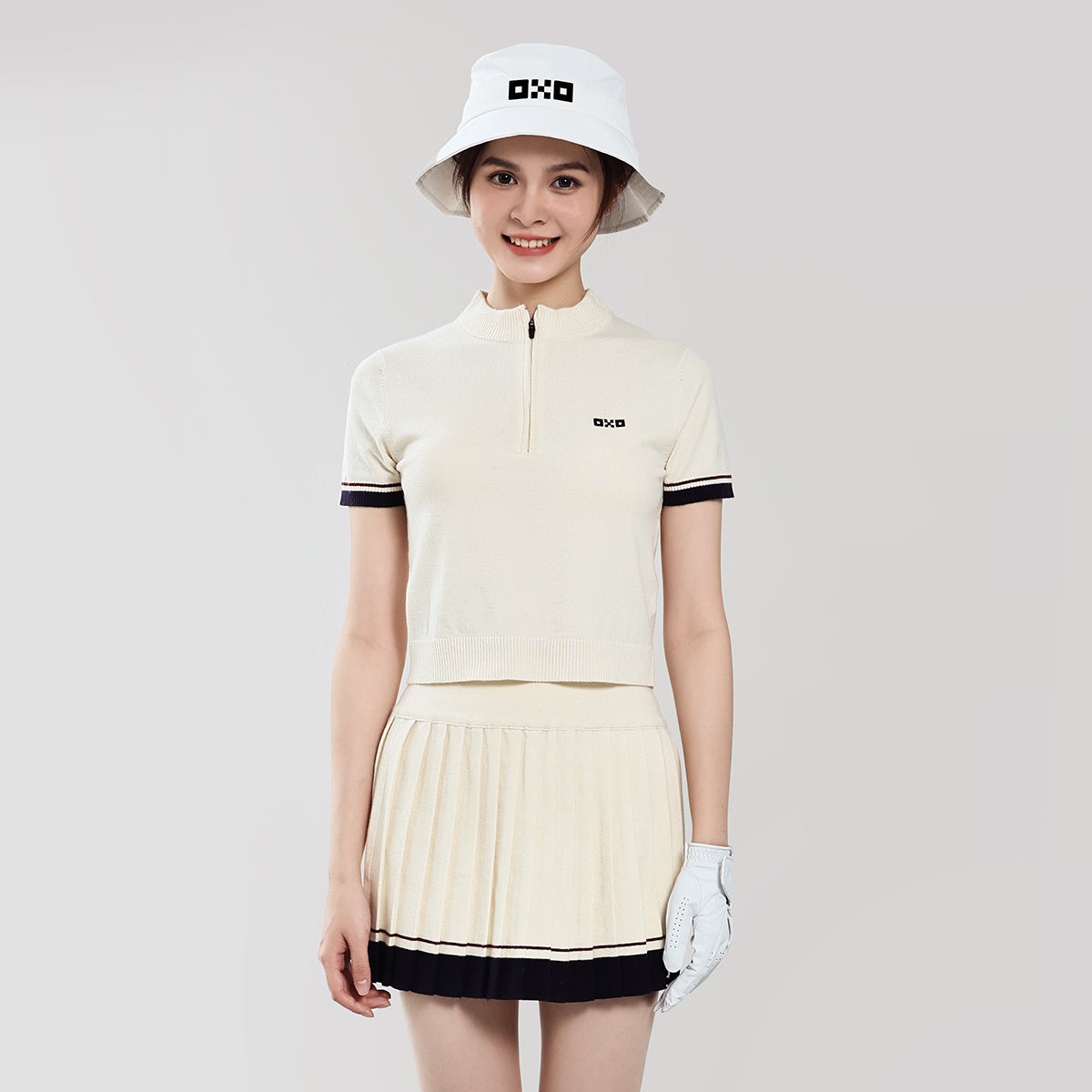 Woman wearing a beige golf outfit with a white hat on a light gray background