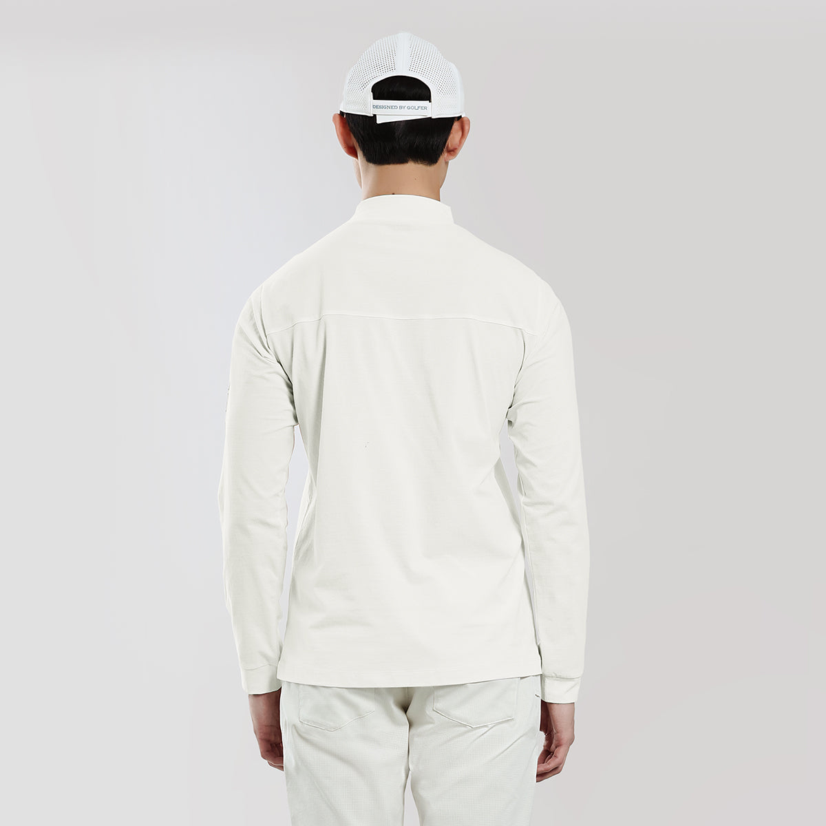 Person wearing a white long-sleeve shirt and pants with a white cap on a light gray background