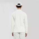 Person wearing a white long-sleeve shirt and pants with a white cap on a light gray background