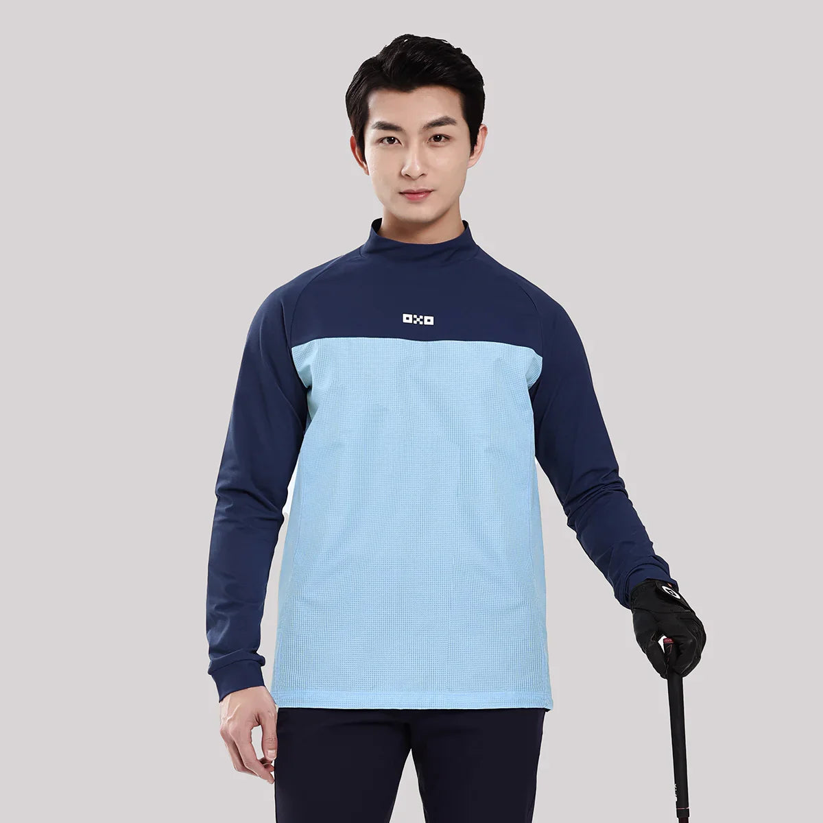 Man wearing a blue and navy long-sleeve shirt with a logo on a gray background