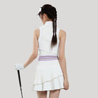 Woman in a white tennis outfit with a skirt holding a tennis racket on a light gray background