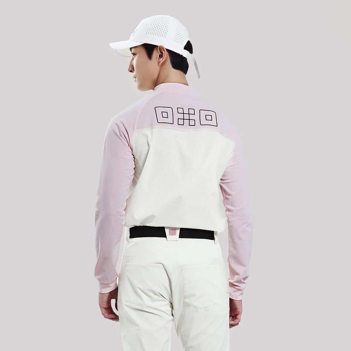 Person wearing a light pink and white long-sleeve shirt with a logo on the back, standing against a plain background.