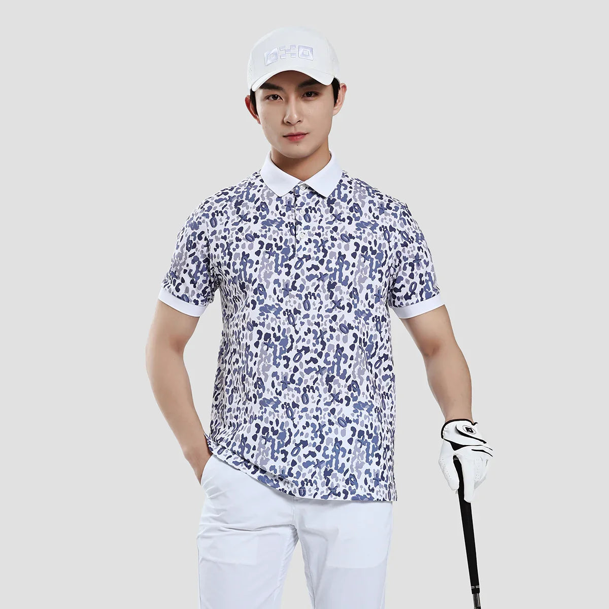 Person wearing a patterned shirt and white pants, holding a golf club on a plain background