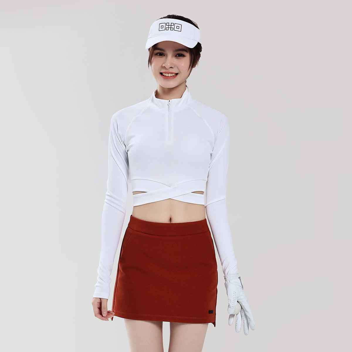 Woman wearing a white long-sleeve top and red skirt with a white visor on a plain background