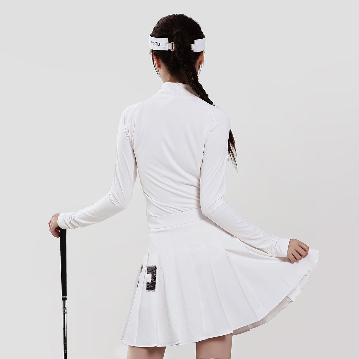 Woman wearing a white tennis dress with a headband and holding a tennis racket on a light gray background