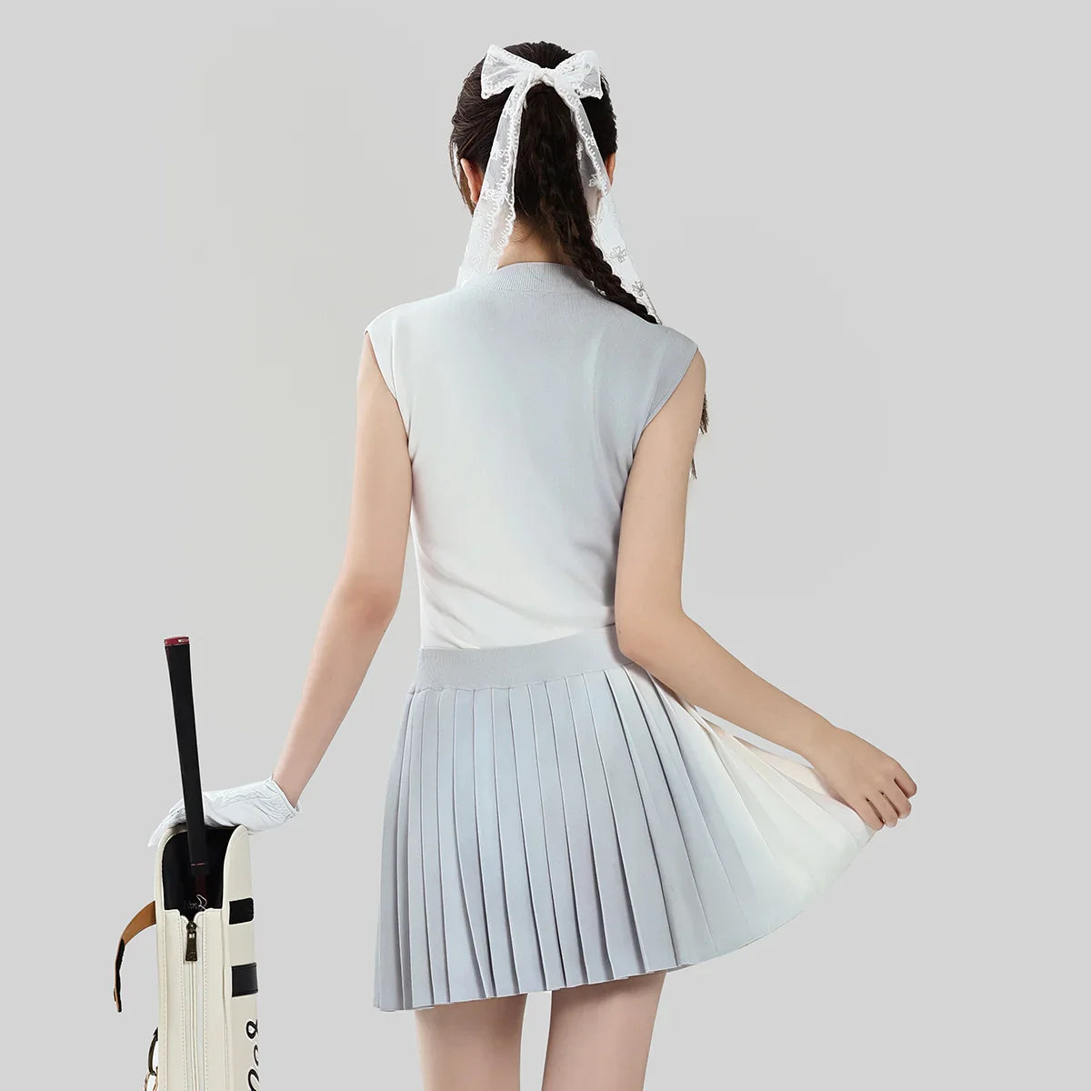 Woman in a light blue outfit with a pleated skirt holding a golf club on a plain background