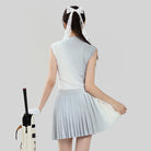 Woman in a light blue outfit with a pleated skirt holding a golf club on a plain background