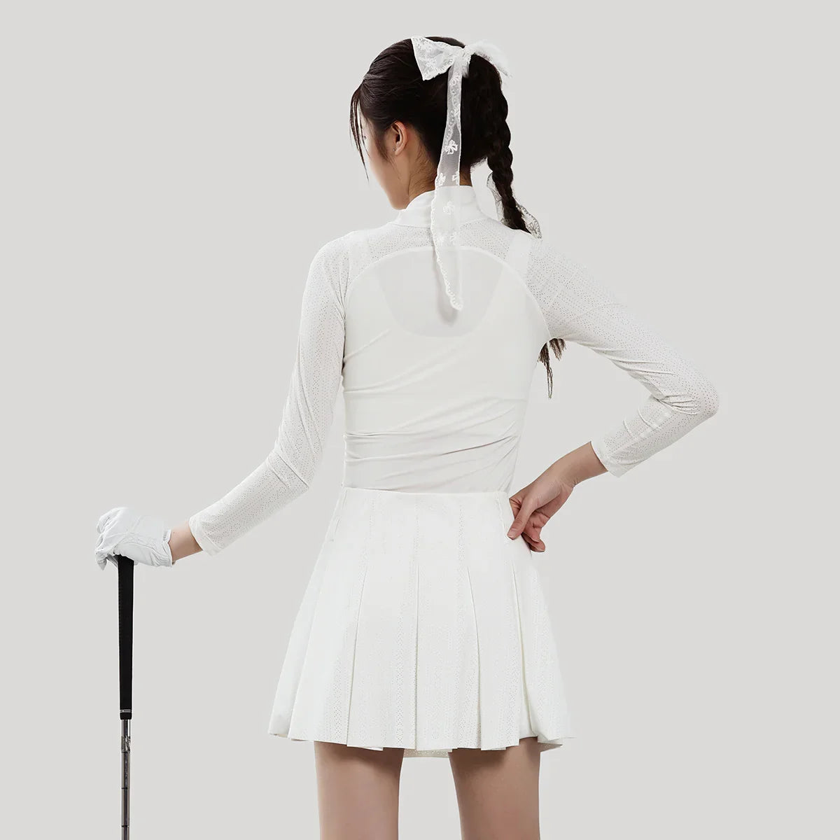 Person wearing a white outfit with a pleated skirt and long-sleeve top on a plain background