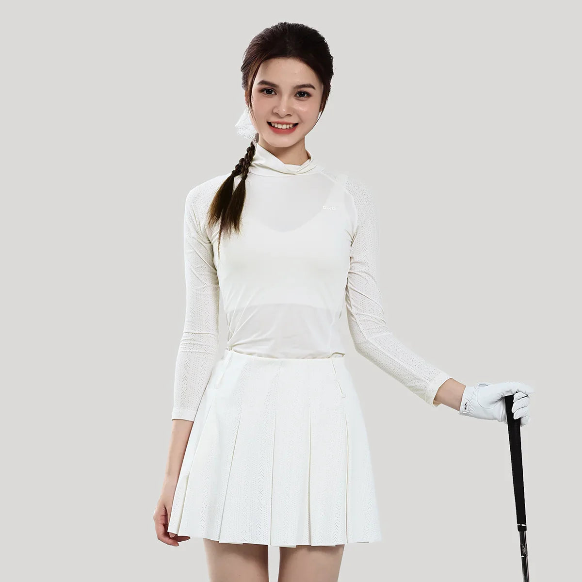 Woman in a white outfit with a skirt, long-sleeve top, and gloves holding a golf club on a plain background