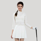 Woman in a white outfit with a skirt, long-sleeve top, and gloves holding a golf club on a plain background