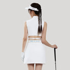 Woman in white golf outfit with visor and club on a light gray background