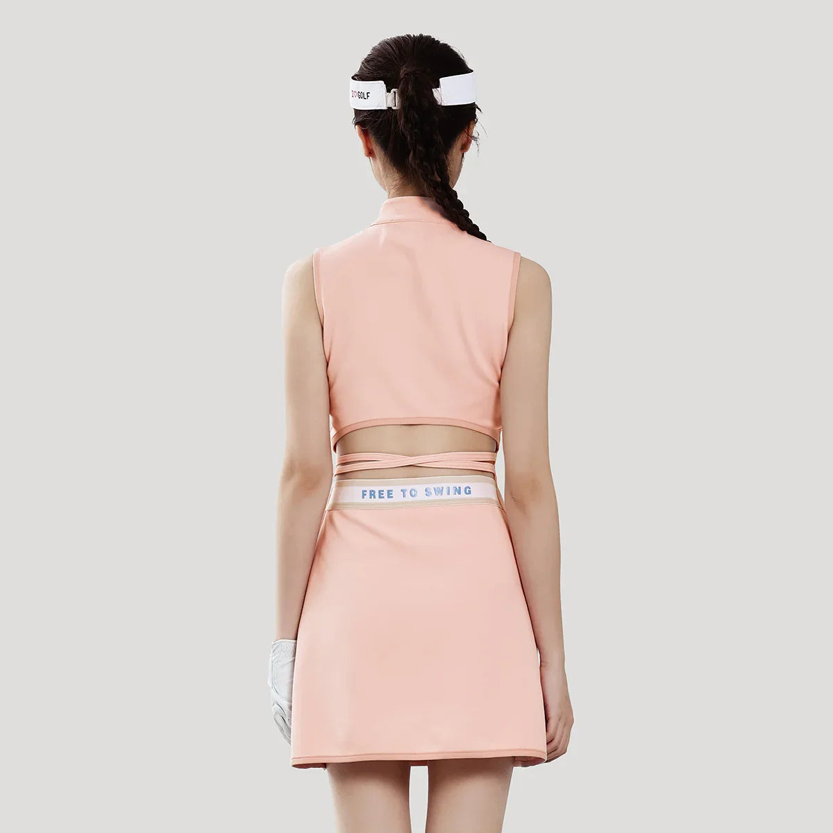 Woman wearing a pink golf outfit with a visor on a light gray background