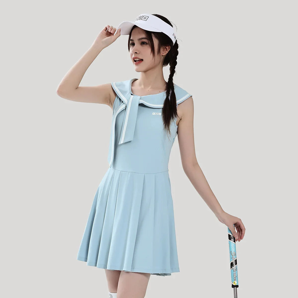 Woman in a light blue dress with a white visor and a golf club on a plain background