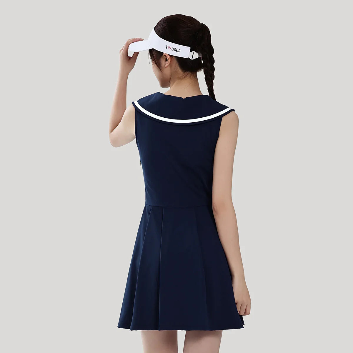 Woman wearing a navy dress with a white collar and visor on a light gray background
