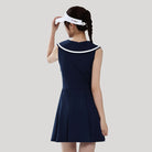 Woman wearing a navy dress with a white collar and visor on a light gray background