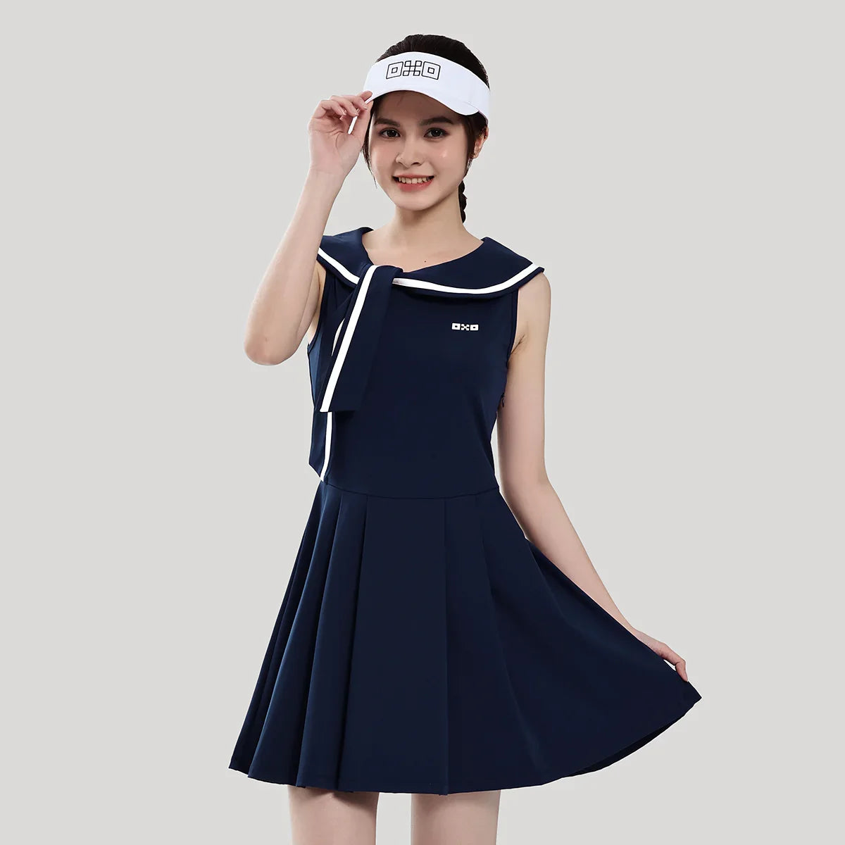 Woman wearing a navy blue dress with white trim and a visor on a light gray background