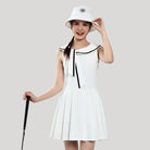 Woman wearing a white dress with black trim and a matching hat on a plain background