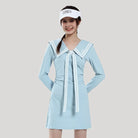 Woman wearing a light blue dress with a white collar and a visor on a plain background