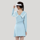 Person wearing a light blue dress with a white visor on a plain background