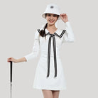 Woman wearing a white dress with black accents and a matching hat, holding a golf club.