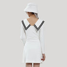 Person wearing a white dress with black trim and a matching hat on a plain background