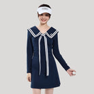 Woman wearing a navy blue dress with white accents on a gray background