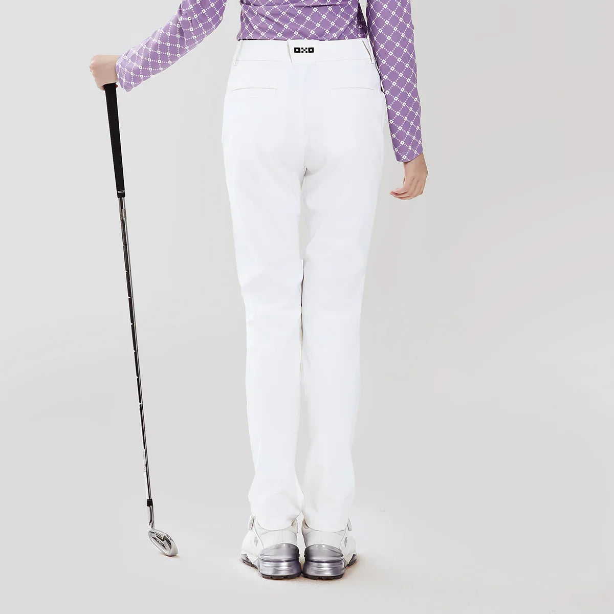 Person wearing white pants and a purple checkered shirt holding a golf club on a light gray background