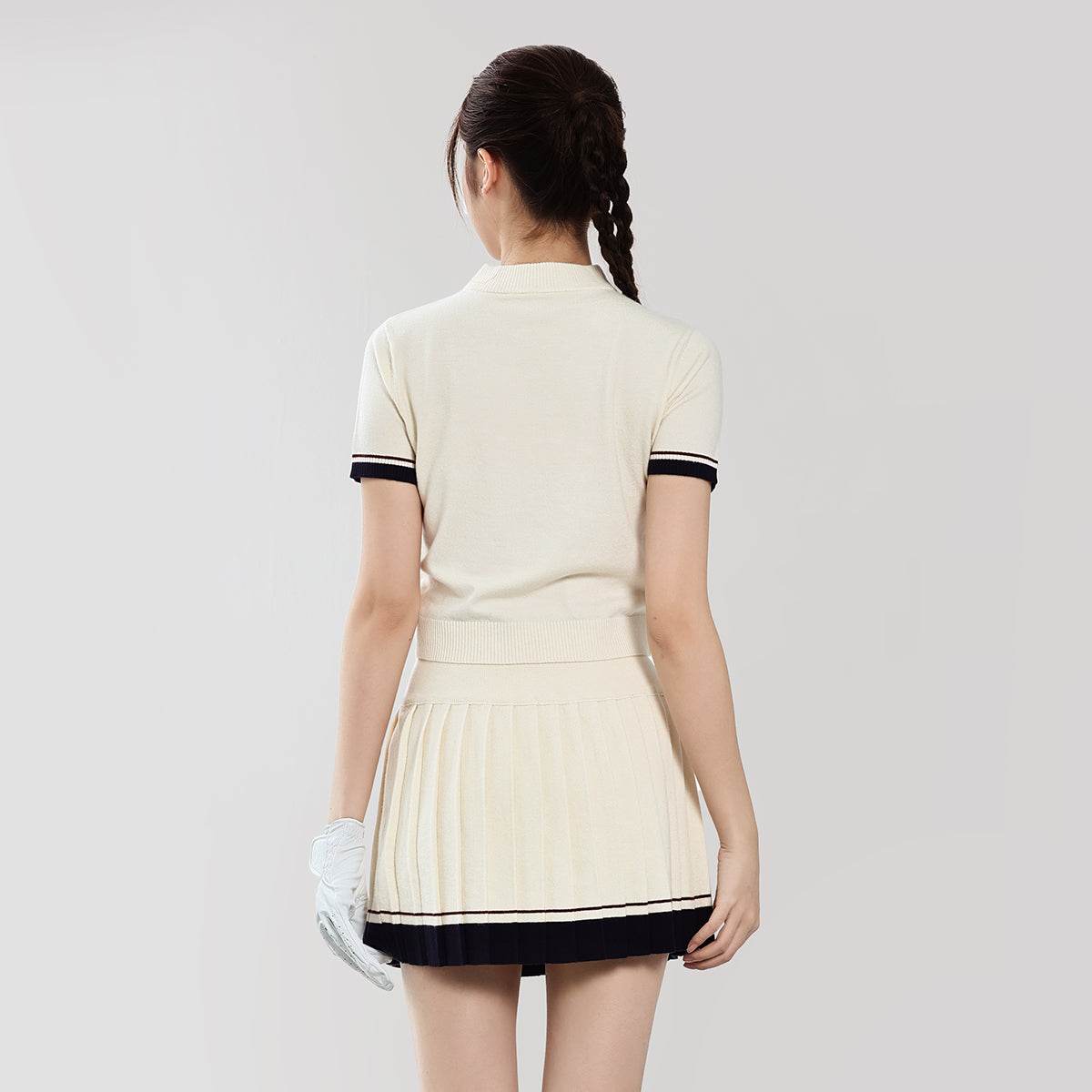 Woman wearing a cream-colored dress with black trim on a plain background