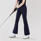 Person wearing navy blue pants and white shoes holding a golf club on a light gray background