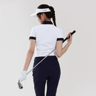 Woman in golf attire holding a golf club against a plain background