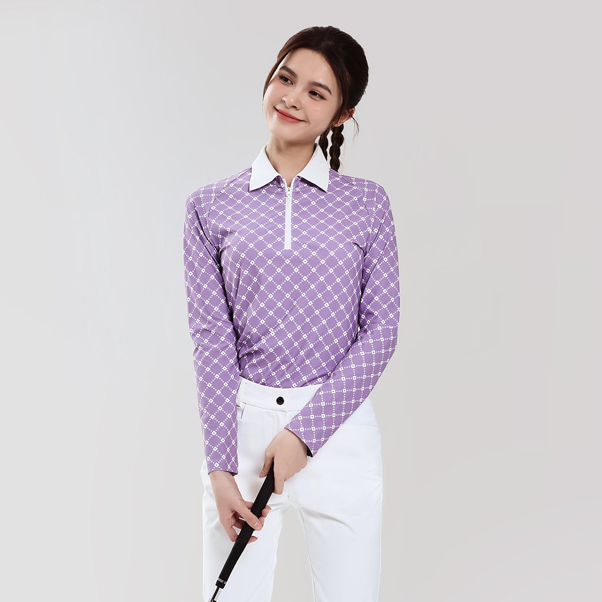 Woman wearing a purple checkered shirt and white pants holding a golf club on a light gray background
