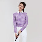 Woman wearing a purple checkered shirt and white pants holding a golf club on a light gray background