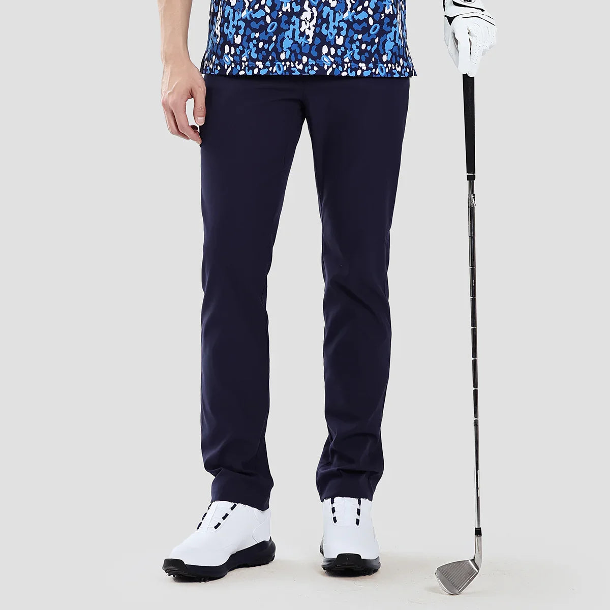 Person wearing navy golf pants with a golf club on a light gray background