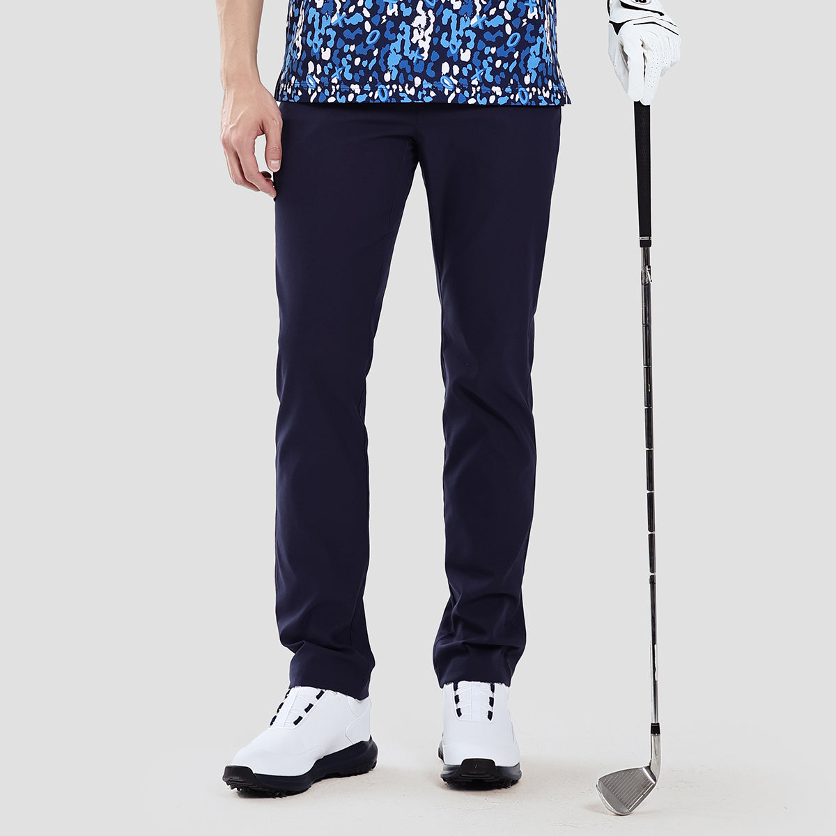 Person wearing navy golf pants with a golf club on a light gray background