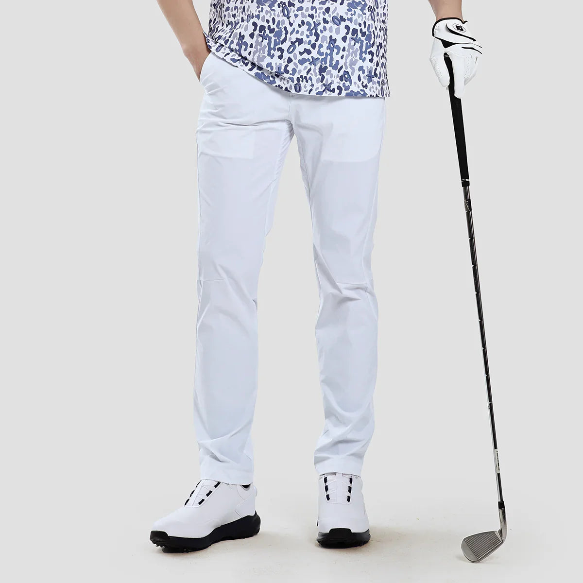 Person wearing white pants and a patterned shirt, holding a golf club on a plain background