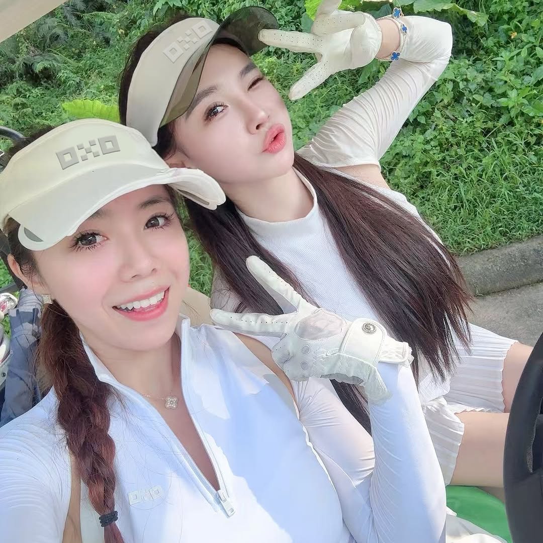Two women posing outdoors, wearing golf hats and gloves.